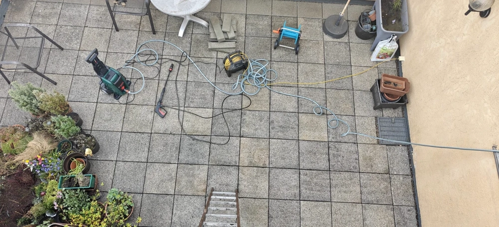 Vogelperspektive auf gepflasterte Terrasse mit Gartengeräten, Kabeltrommel und Topfpflanzen bei Terrassensanierung