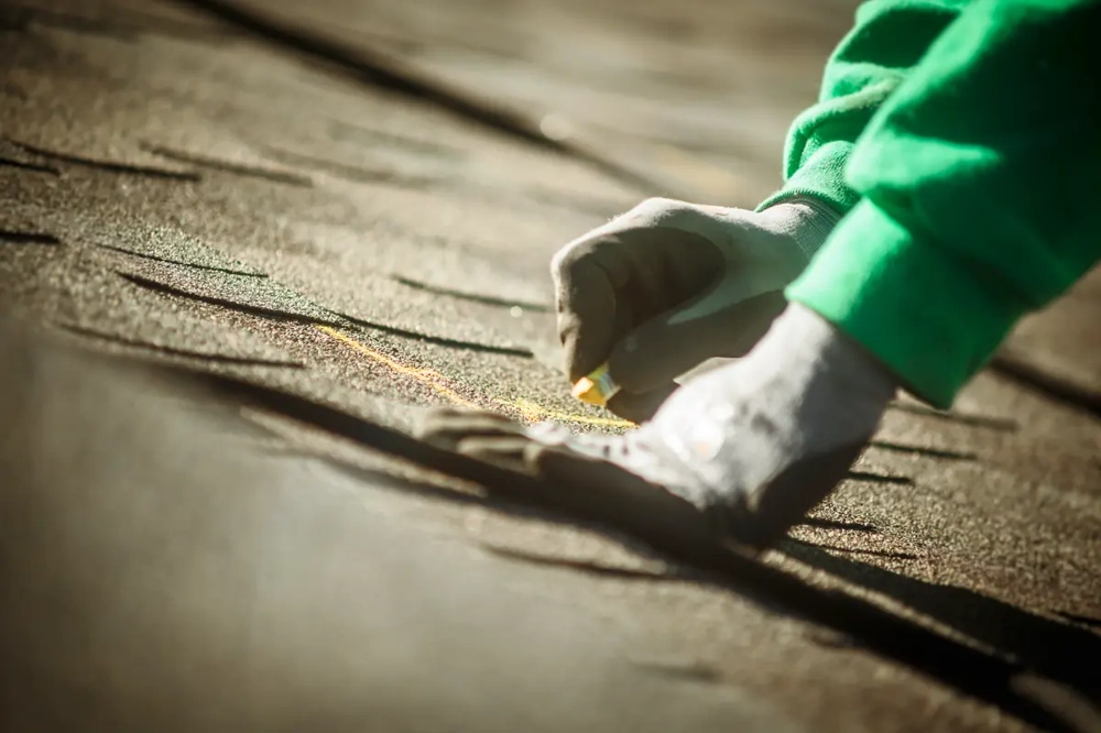 Hand in Arbeitshandschuh markiert mit Kreide eine Linie auf Bitumenschindeln