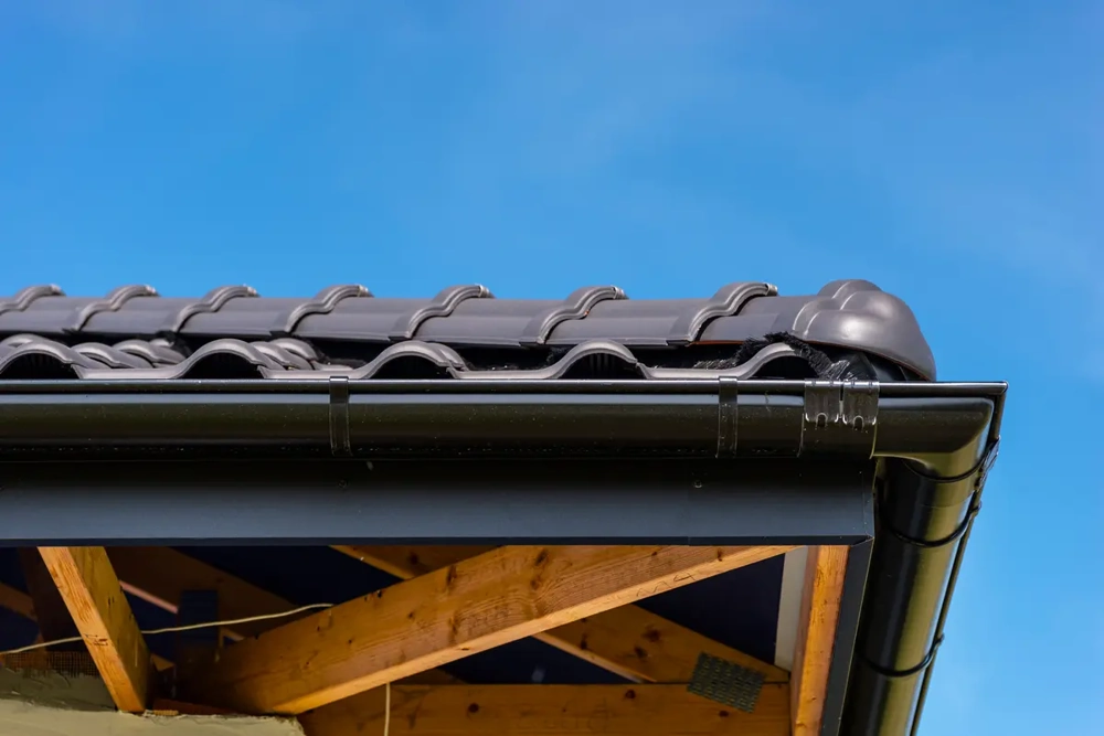 Detail einer schwarzen Dachrinne an Ziegeldach mit sichtbaren Dachsparren – Dachrinnen Montage