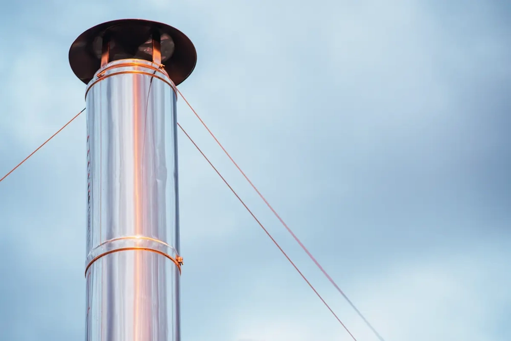 Metallene Kaminverkleidung mit Abspannseilen vor bewölktem Himmel