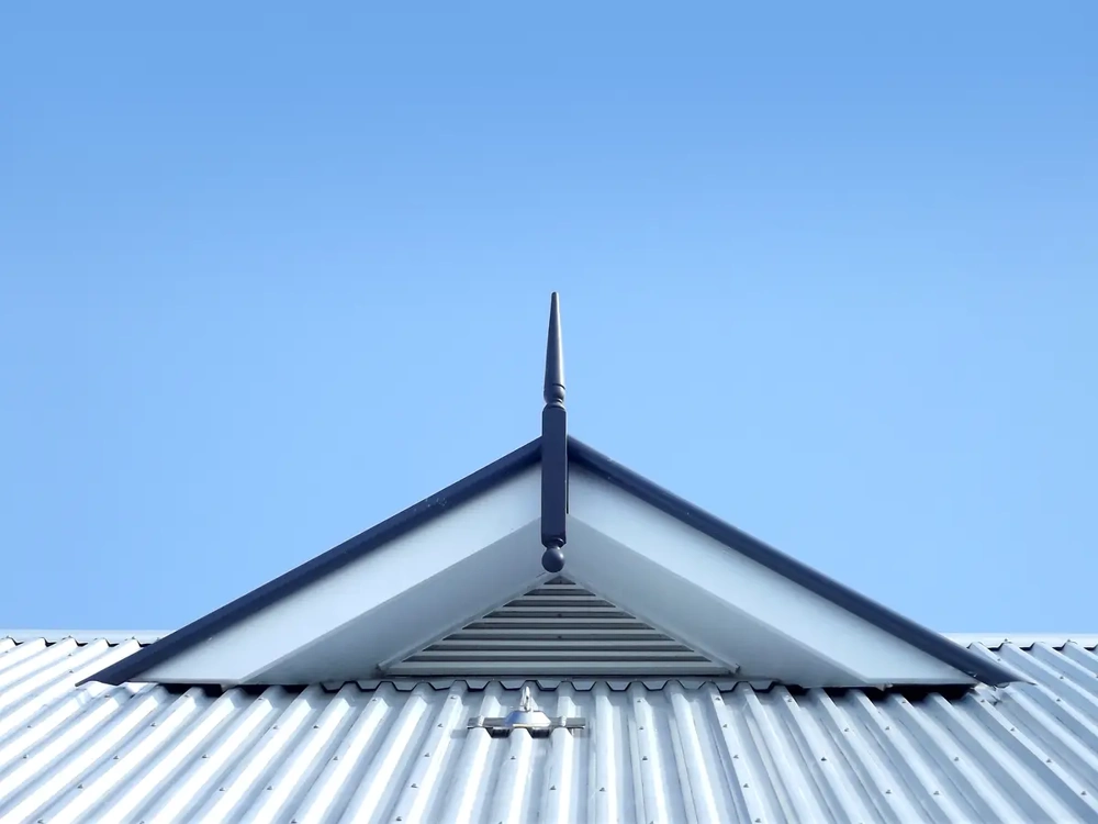 Trapezblech Dach mit Giebelgaube und Lüftungsgitter vor blauem Himmel