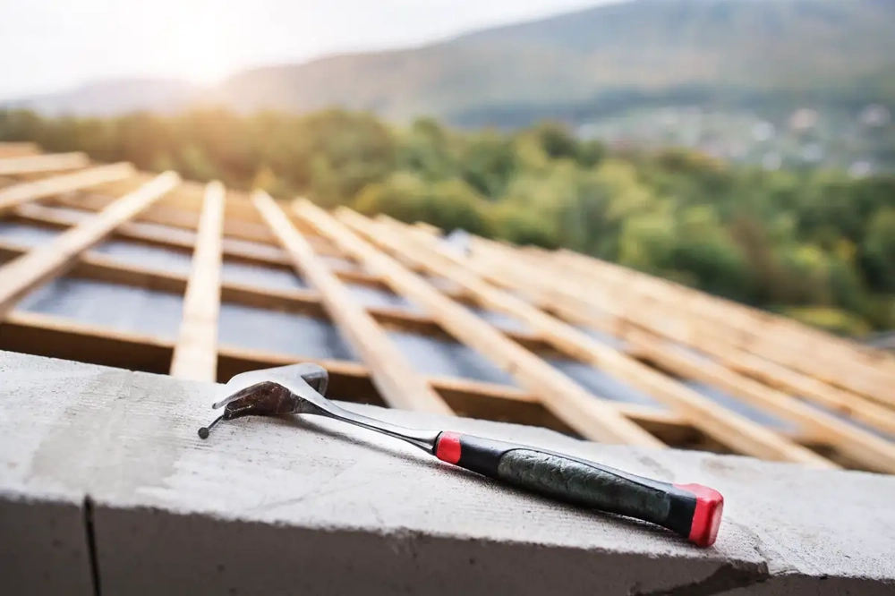 Hammer liegt auf Holzlatten eines entblößten Daches – Vorbereitung für Dachreparatur