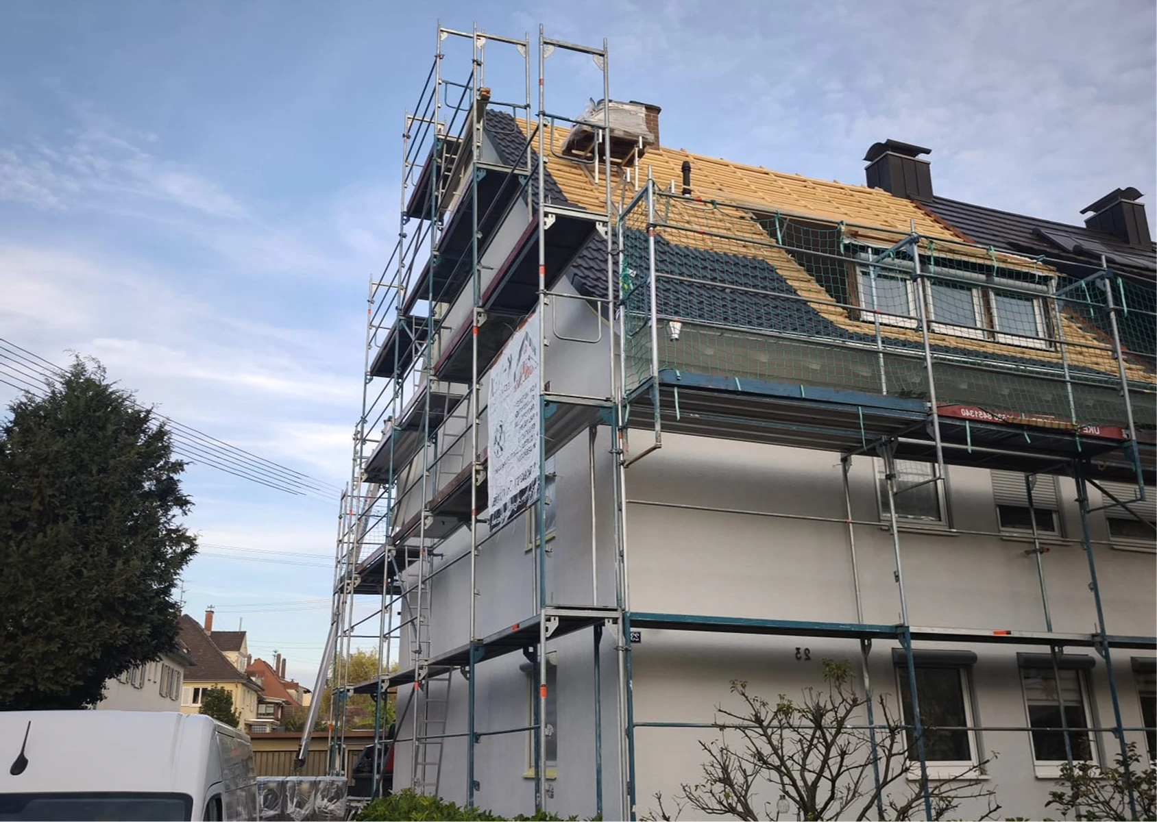 Eingerüstetes Wohnhaus während Dachsanierung mit freigelegtem Dachstuhl und halb neu gedecktem Ziegeldach