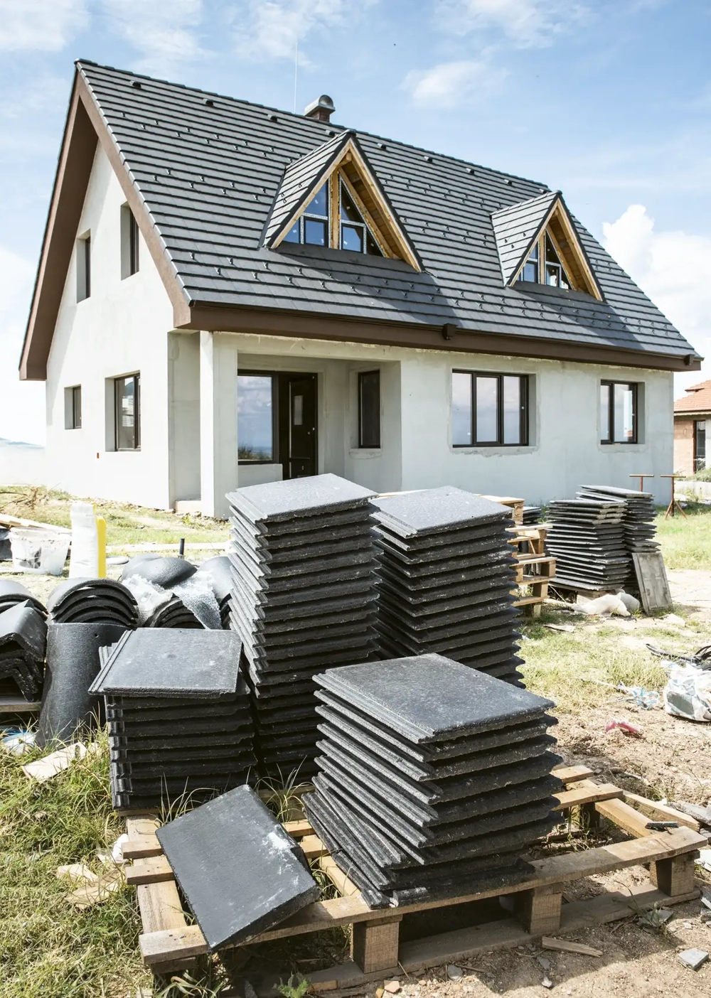 Gestapelte Dachziegel vor Einfamilienhaus im Rahmen der Dacheindeckung