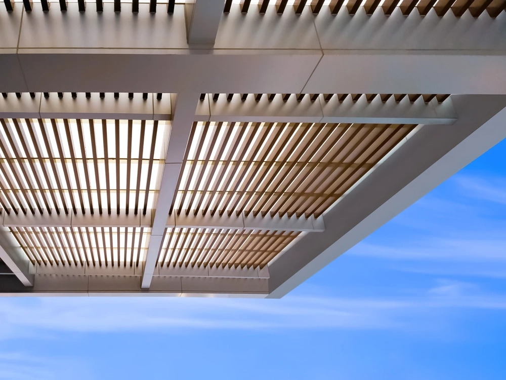 Moderne Terrassenüberdachung mit Holzlamellen und Stahlträgern vor blauem Himmel