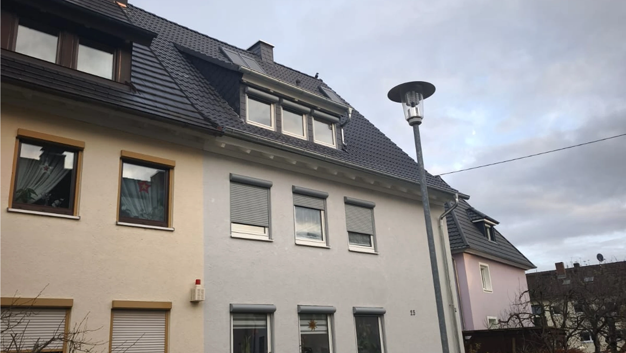 Frisch eingedecktes Ziegeldach mit Gaubenfenstern und Regenrinne an modernisierter Wohnhausfassade