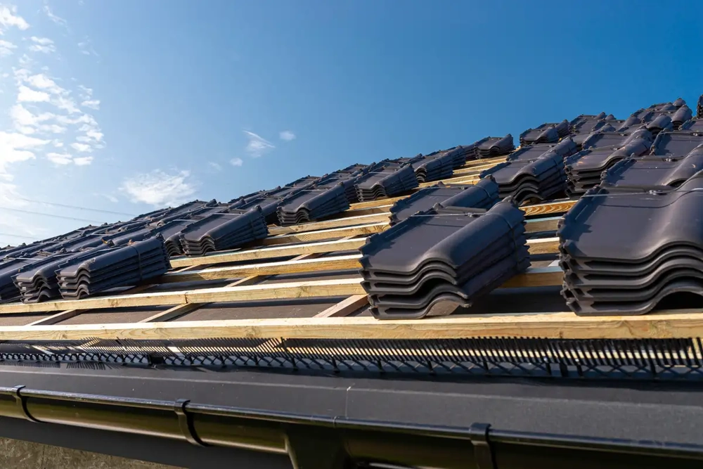 Stapelweise dunkle Dachziegel auf Holzlattung für Ziegeldach unter klarem Himmel