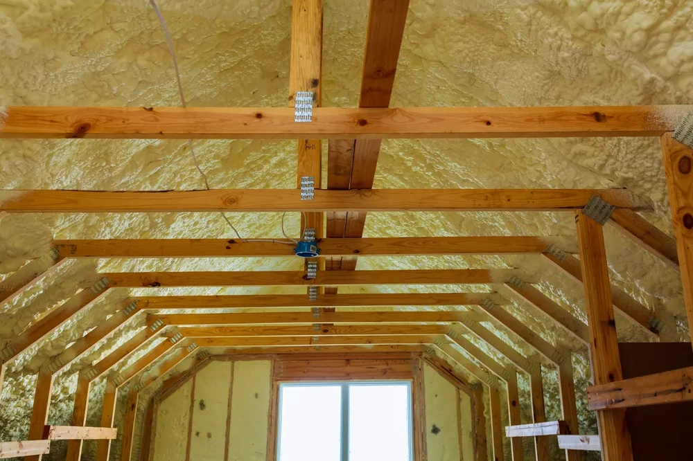 Innenansicht eines Dachstuhls mit aufgespritzter Schaum-Dachdämmung zwischen Holzbalken