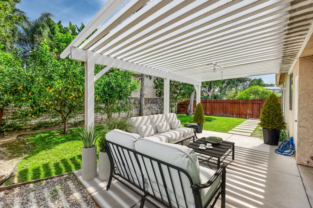 Weißer gepolsterter Lounge-Bereich unter Holzlatten-Terrassenüberdachung mit Gartenblick
