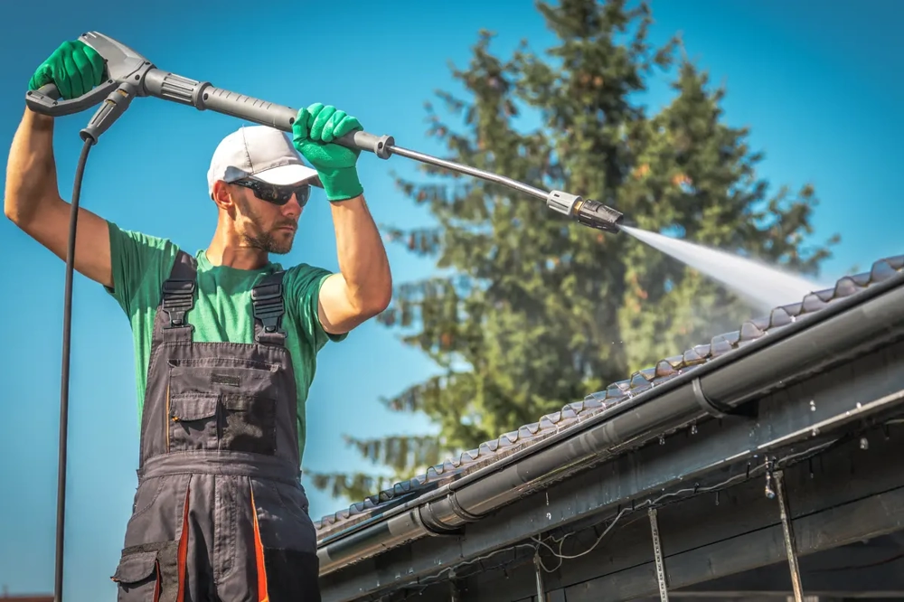 Dachreinigung durch Handwerker mit Hochdruckreiniger auf Ziegeldach und Dachrinne