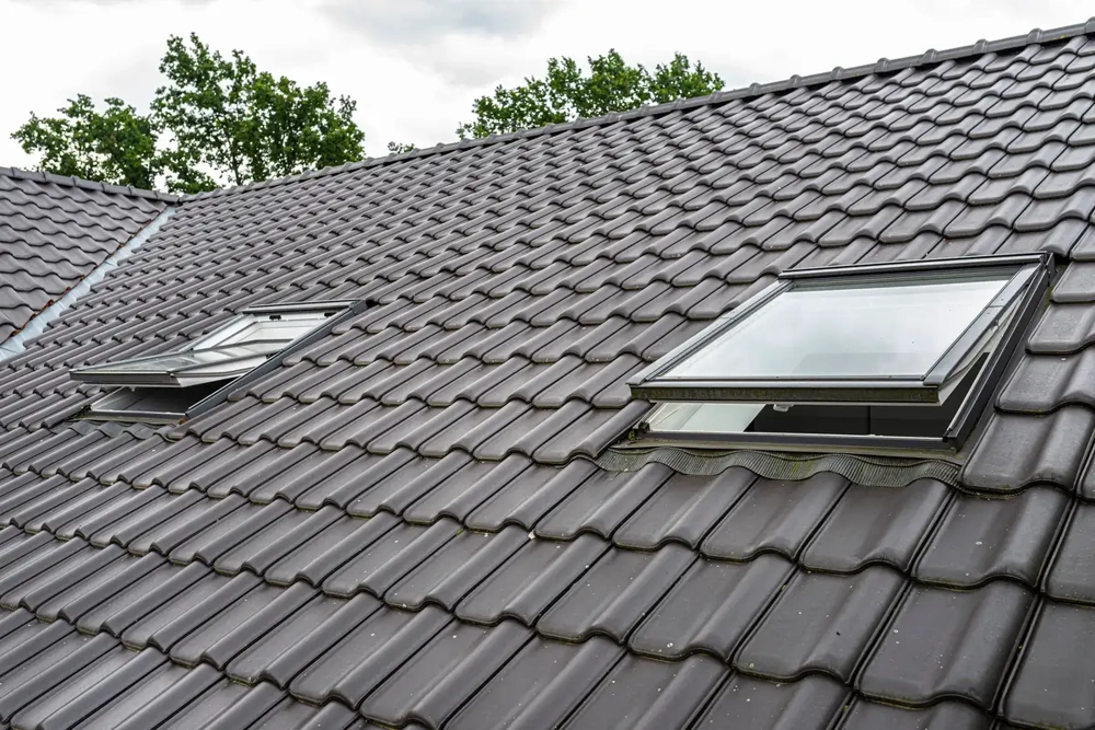 Dunkles Ziegeldach mit zwei geöffneten Dachfenstern und moderner Tonziegeleindeckung
