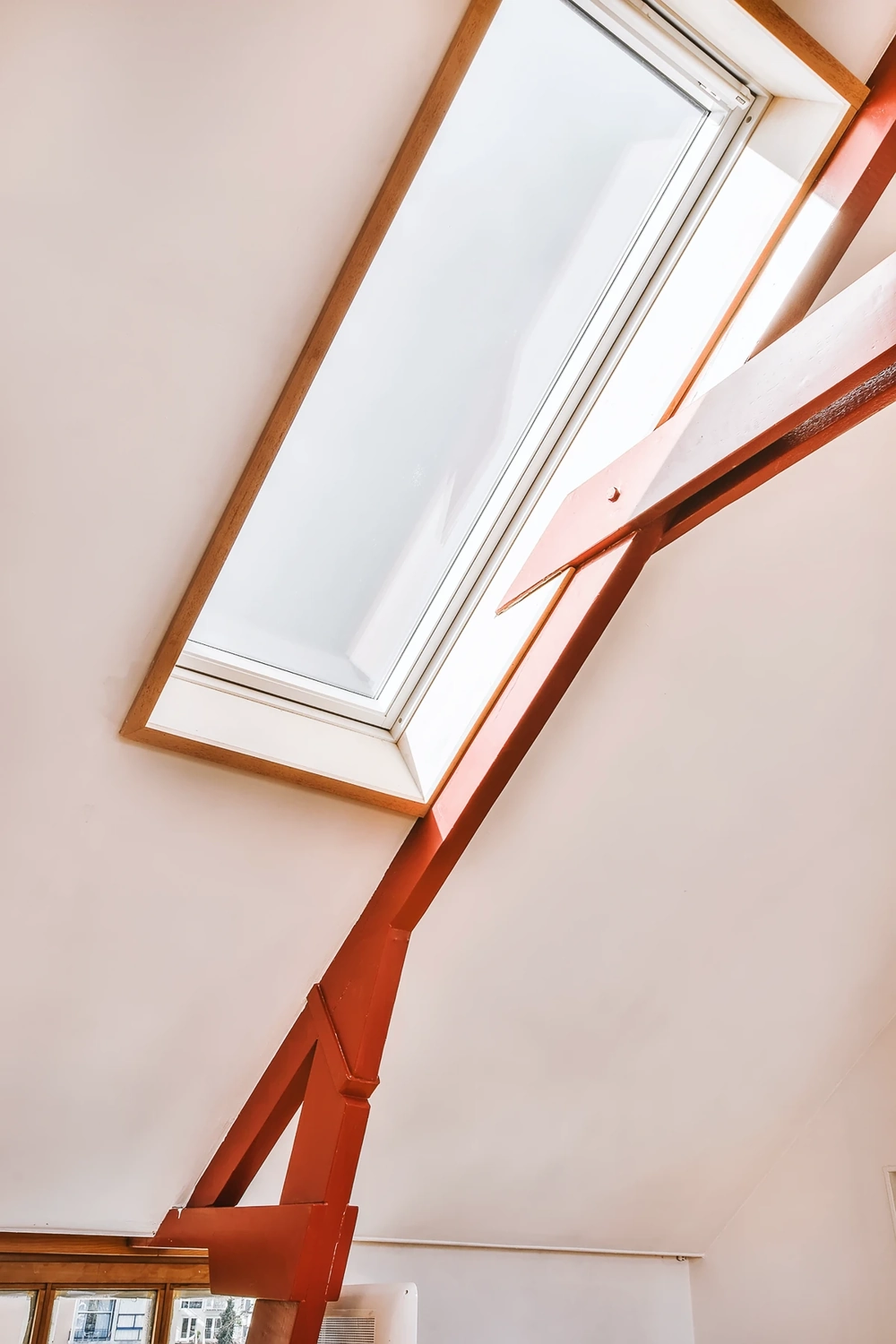 Dachfenster mit weißem Rahmen in schräger Decke und rotem Stahlträger